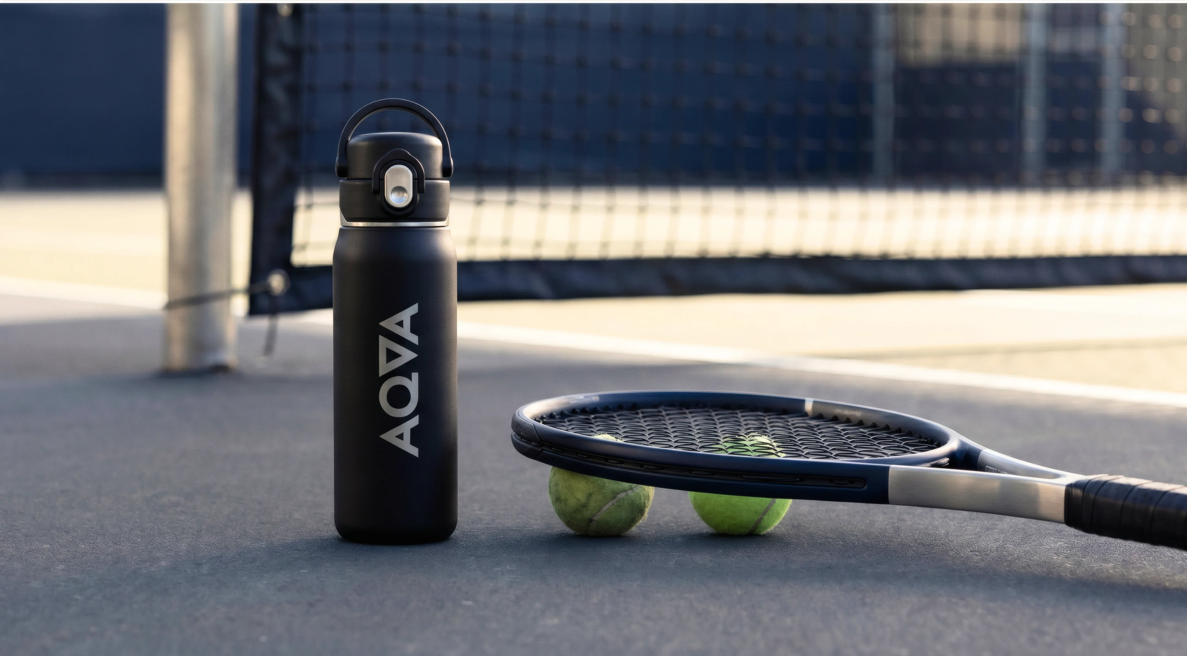 Black AQVA bottle on a tennis court beside a racket and balls