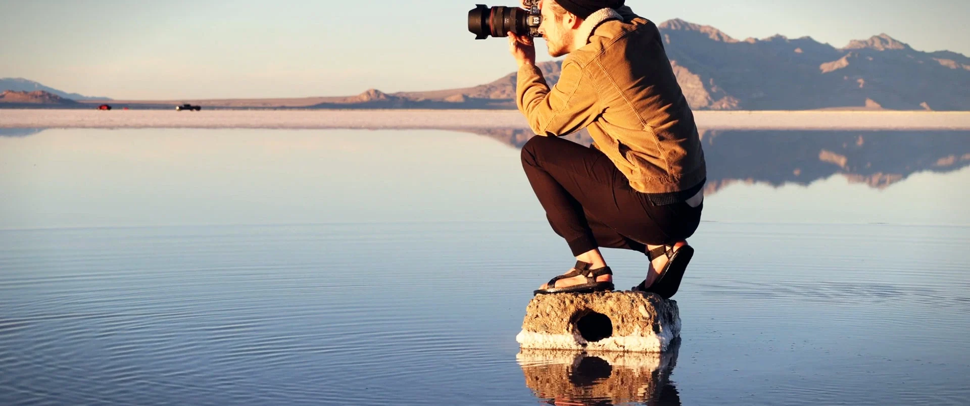 A photographer crouching on a mirror-like lake
