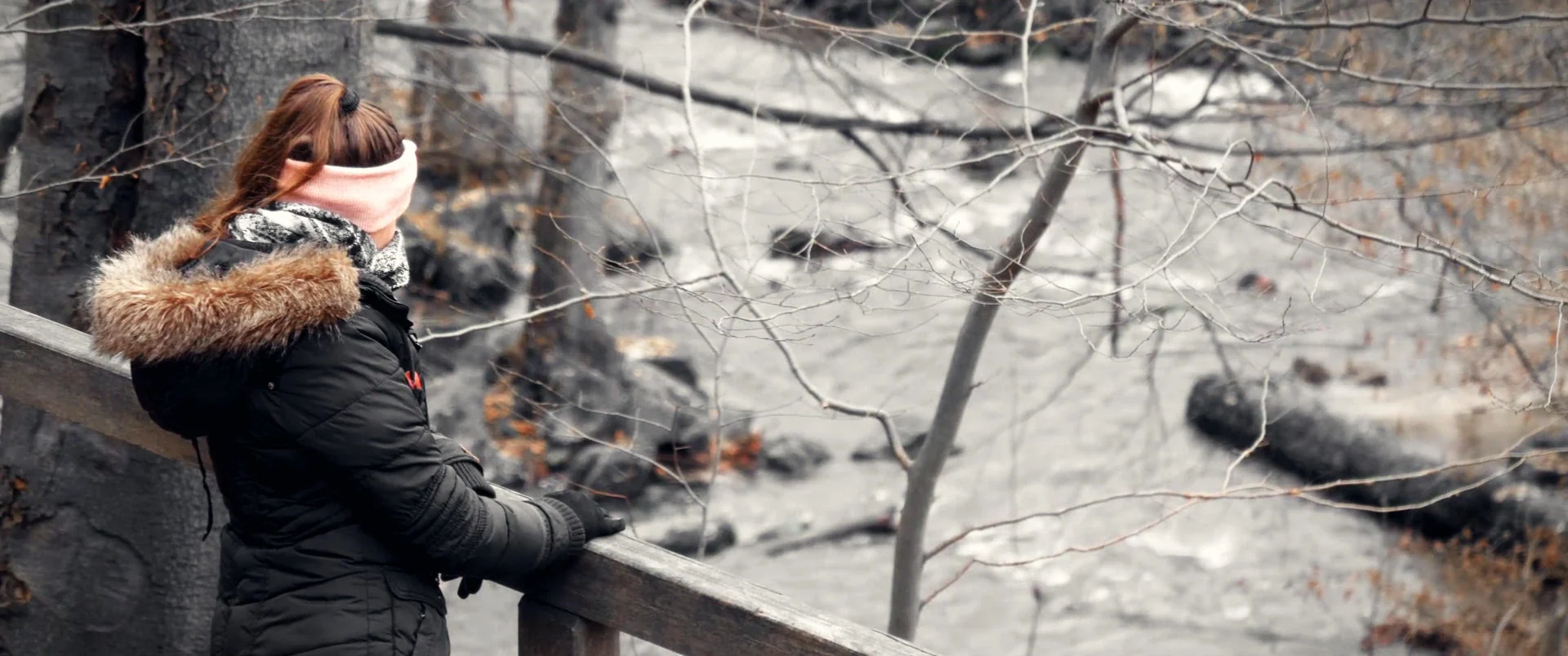 A woman in a winter coat looking over a river
